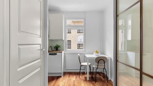 Een compacte keuken met witte kasten, een houten vloer en een raam met uitzicht op gebouwen.
