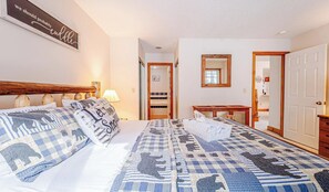 Un dormitorio con una cama grande, un cabecero de madera, una mesita de noche, una lámpara, un espejo y una puerta que da a un baño.
