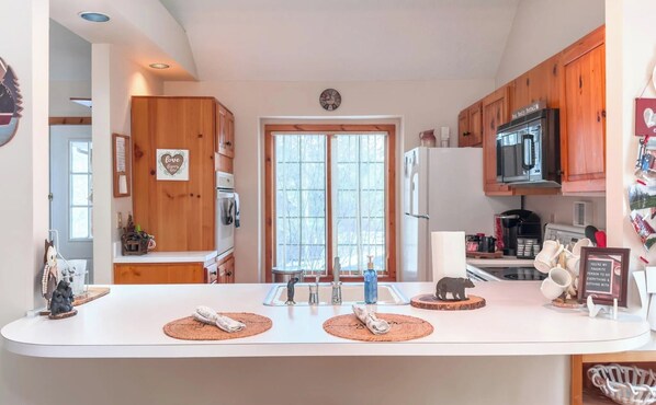 A kitchen with wooden cabinets, a white countertop, a microwave, and a refrigerator.