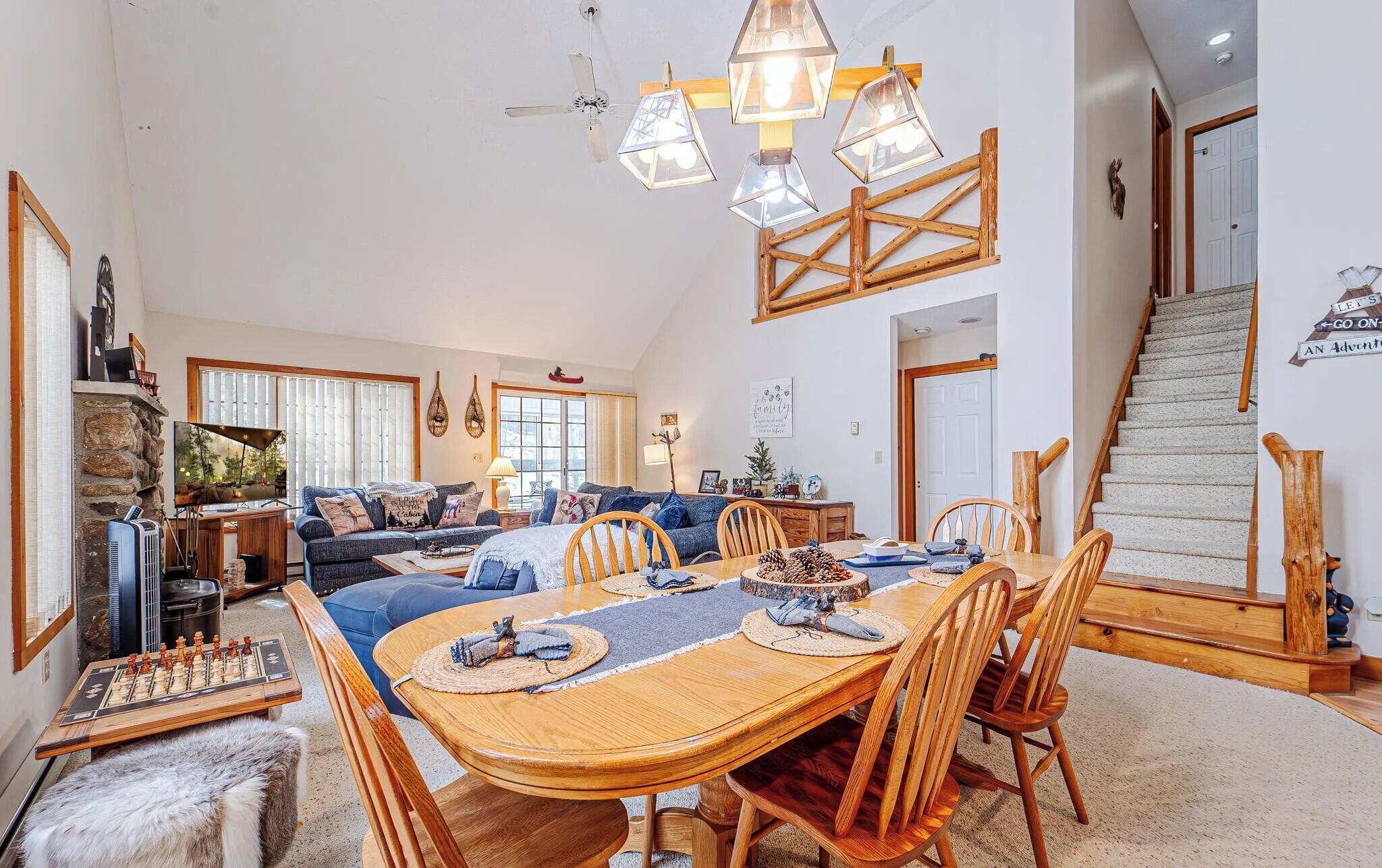 A spacious living room with a large wooden dining table, comfortable seating, and a staircase leading to an upper level.