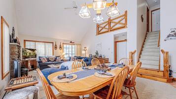 A spacious living room with a large wooden dining table, comfortable seating, and a staircase leading to an upper level.