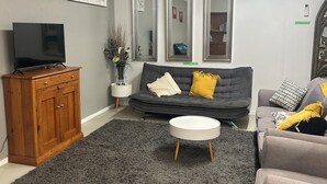 Ein Wohnzimmer mit grauem Sofa, einem runden Couchtisch, einer Holzkabine und einem Flachbildfernseher.