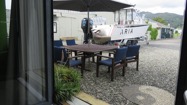 Ein Essbereich mit Tisch und Stühlen, ein Boot in der Nähe und Blick auf eine gebirgige Landschaft.