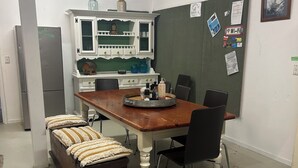 Eine kleine Küche mit Holztisch, Stühlen, einem Kühlschrank und einer grünen Wand mit verschiedenen Nachrichten.