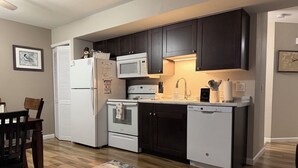 A kitchen with dark cabinets, a white refrigerator, a microwave, an oven, and a dishwasher.
