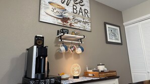 A coffee bar setup with a coffee machine, mugs, and a sign that reads 'Coffee Bar Love Brewed Here'.