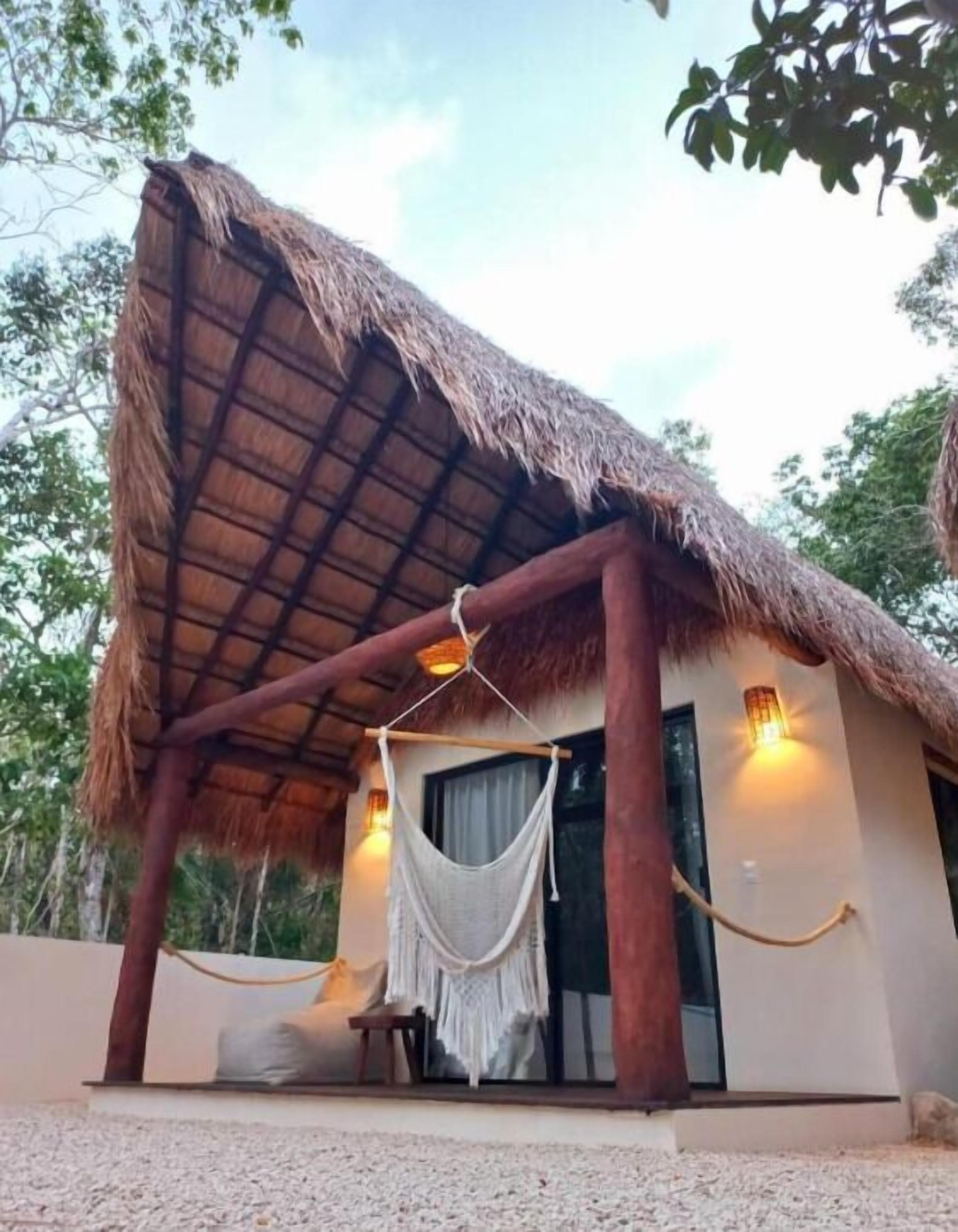 A thatched-roof structure with a hanging hammock and a bench, suggesting a relaxing outdoor seating area.