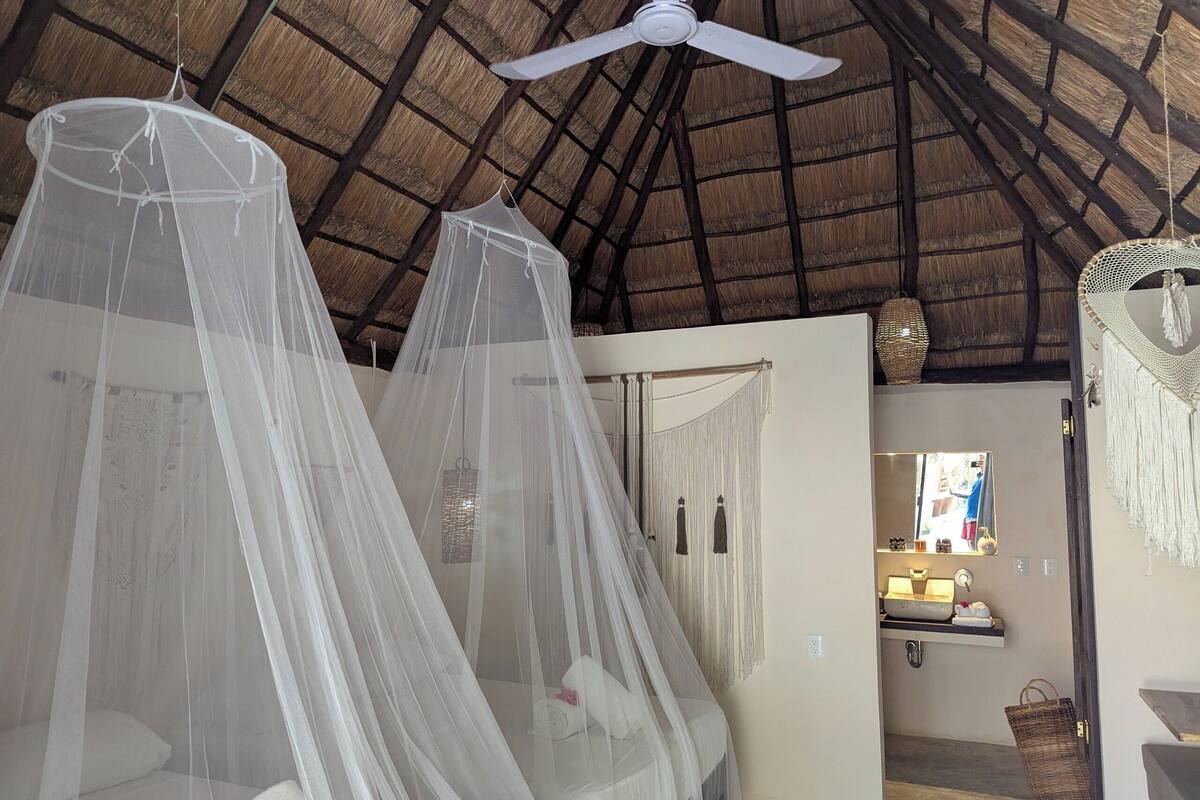 A room with a thatched roof, a ceiling fan, and a bed with a mosquito net.