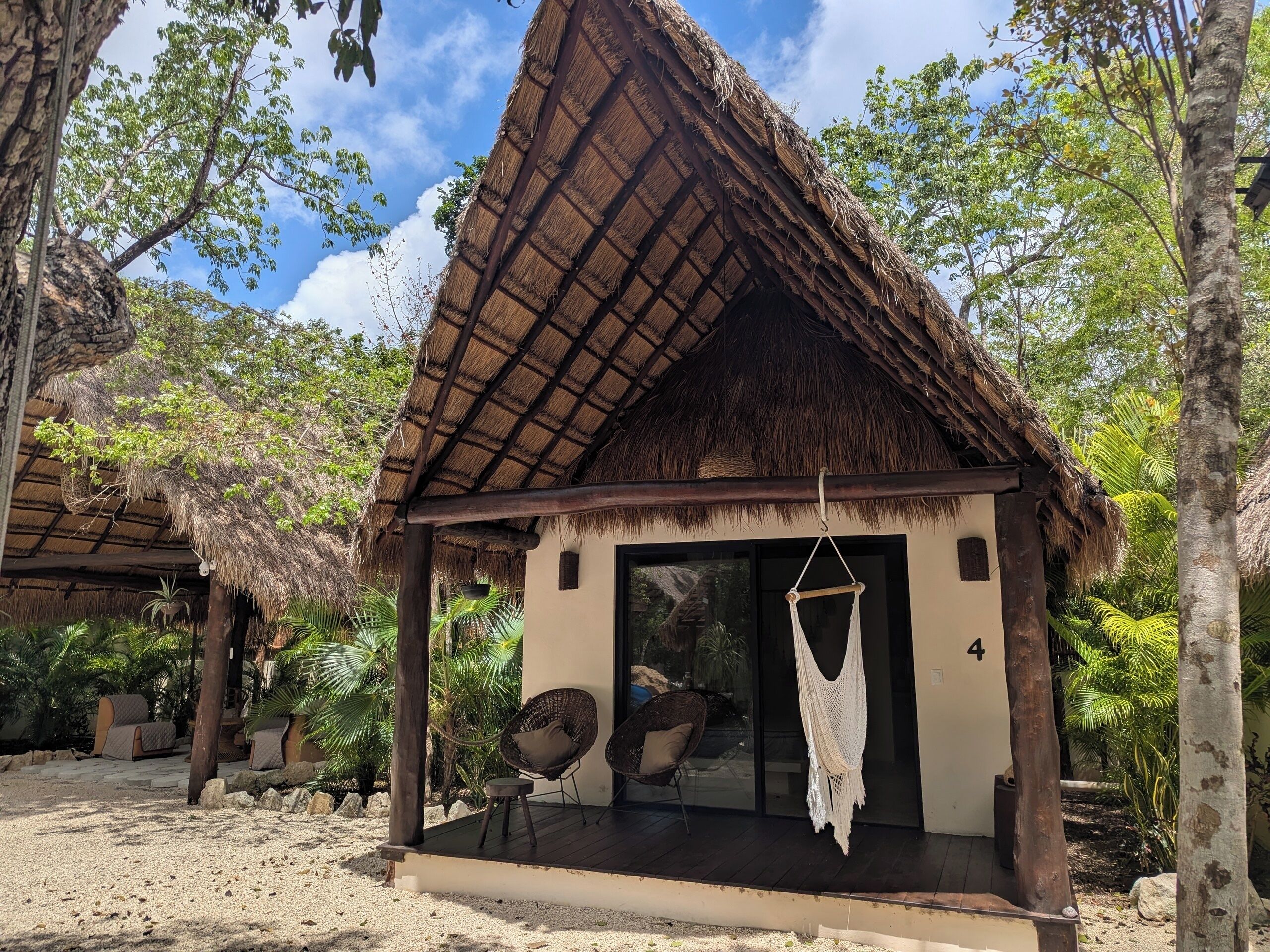 A small, thatched-roof structure with a glass door, surrounded by tropical vegetation.