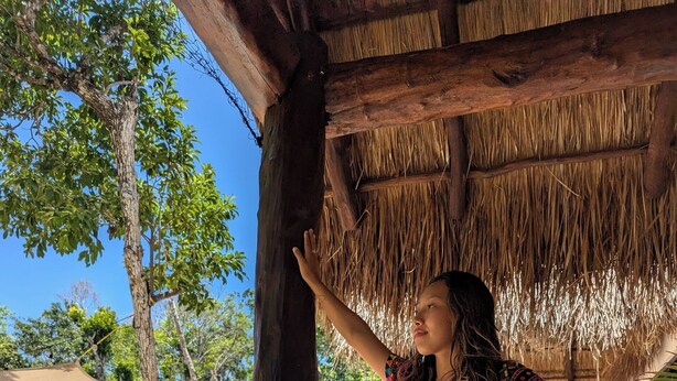 A person standing under a thatched roof structure, with a pool and outdoor seating visible in the background. - Magic Xcacel Tulum (Tulum)