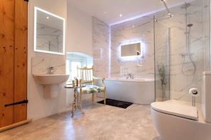 Ein Badezimmer mit Marmorwaschbecken, einer Badewanne, einer Toilette, einer Duschkabine aus Glas und einer Holztür.