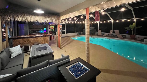 Área interna de piscina com bar, assentos e telhado de palha.