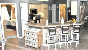 Cozinha moderna com ilha central, banquetas de bar e armário de madeira com gavetas.