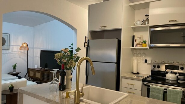 Una cucina moderna con frigorifero, fornello e microonde integrati. C'è un lavello con un rubinetto dorato e un'area pranzo con tavolo e sedie.