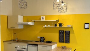 A compact kitchen with a sink, stove, and dishwasher, a wooden table with chairs, and a chalkboard menu listing food items. - Station Apartment West (La Spezia)