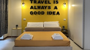 A hotel room with a bed, a yellow wall with a motivational quote, a small table with a plant, and a white wardrobe. - Station Apartment West (La Spezia)