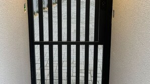 A black metal gate with vertical bars and a mesh screen, leading to a building entrance. - Apartamentos Bora Bora Hospedagens (Joinville)