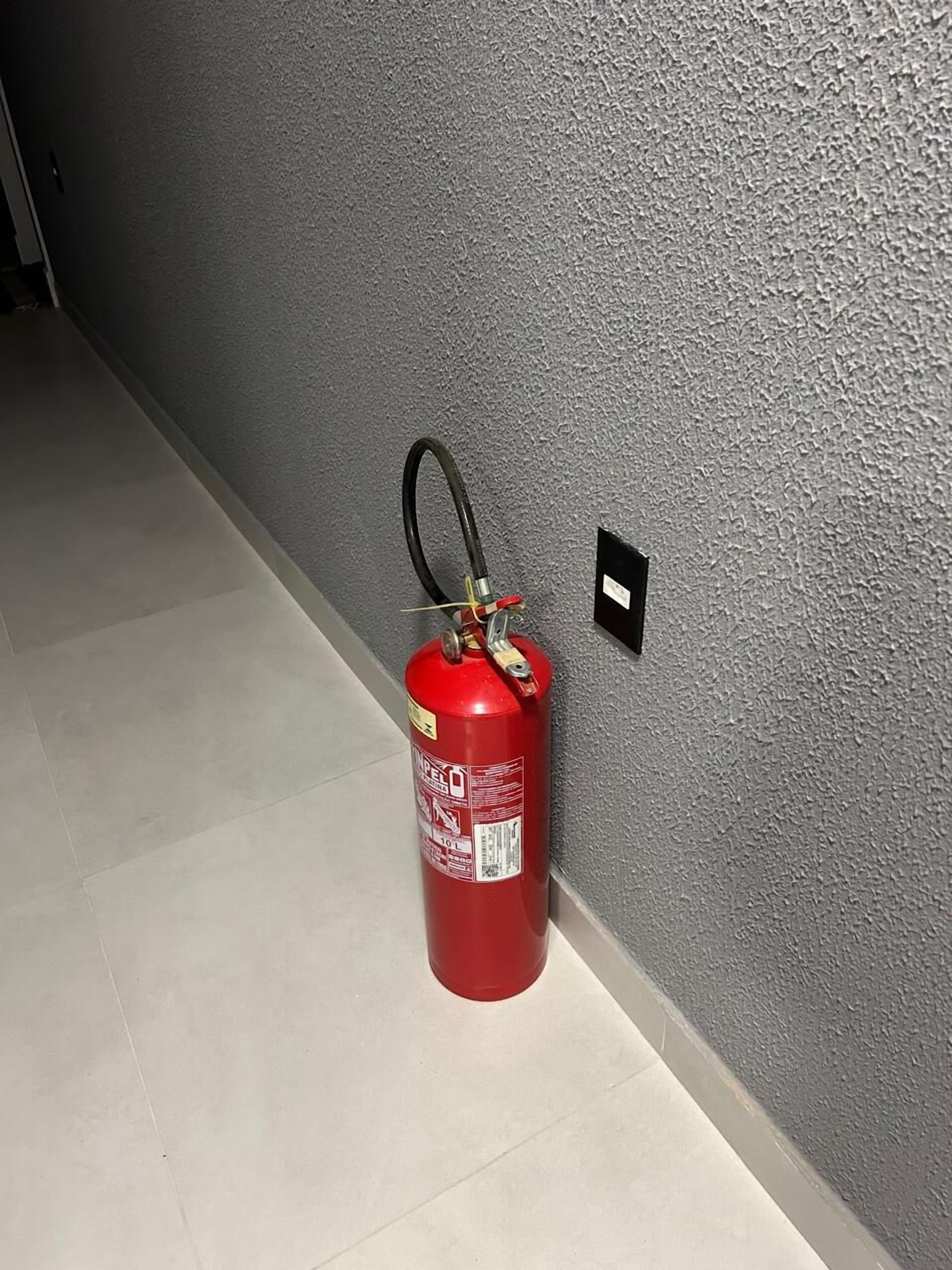 A red fire extinguisher mounted on a textured gray wall in a hallway.