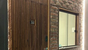A sliding wooden door with a number plate, a window with a view of the outside, and a brick wall. - Apartamentos Bora Bora Hospedagens (Joinville)