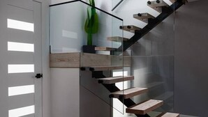 Eine moderne Treppe mit Glastrennwand und Holzboden, die zu einer Plattform mit einer Zimmerpflanze führt.