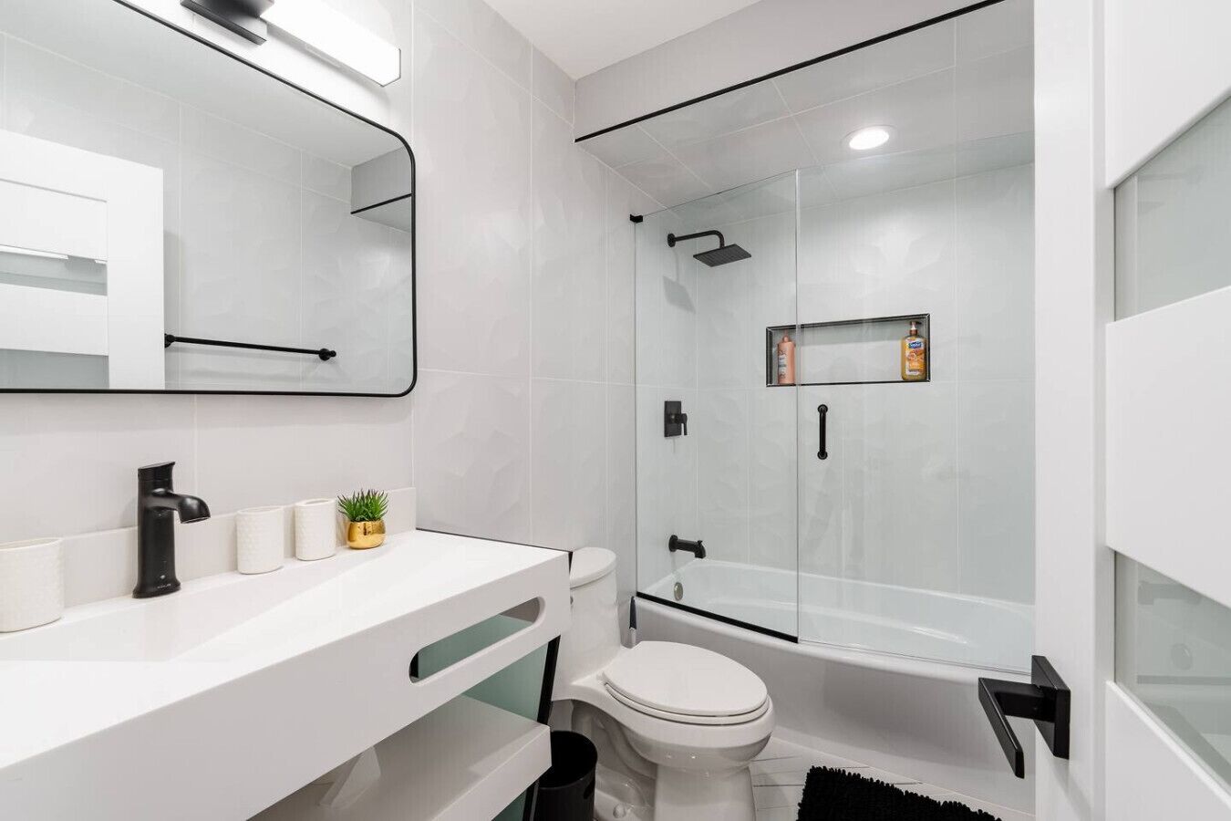 Un bany modern amb un lavabo blanc, un aixeta negra, un vàter i una zona de dutxa amb envà.