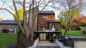 Ein modernes Haus mit einer Terrasse, einem Deck und einem großen Fenster mit Blick auf einen Garten.