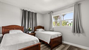 Ein Schlafzimmer mit zwei hölzernen Betten, einem Nachttisch mit Blumenvase und einem Fenster mit Vorhängen.