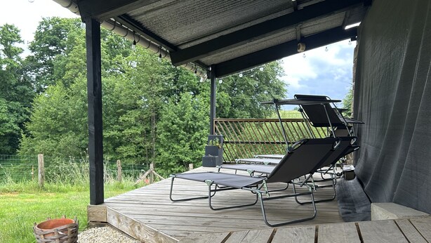 A covered outdoor seating area with wooden tables and chairs, surrounded by gravel and purple flowers.