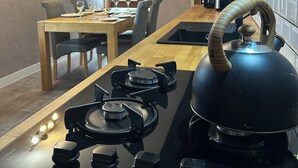 A kitchen with a gas stove, kettle, and a dining area with chairs and a table.