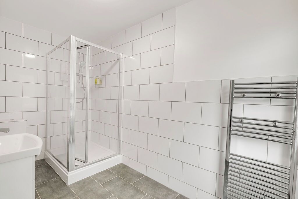 Ein modernes Badezimmer mit weißen Fliesen, einer Duschkabine aus Glas, einem weißen Waschbecken und einem chromfarbenen Handtuchhalter.