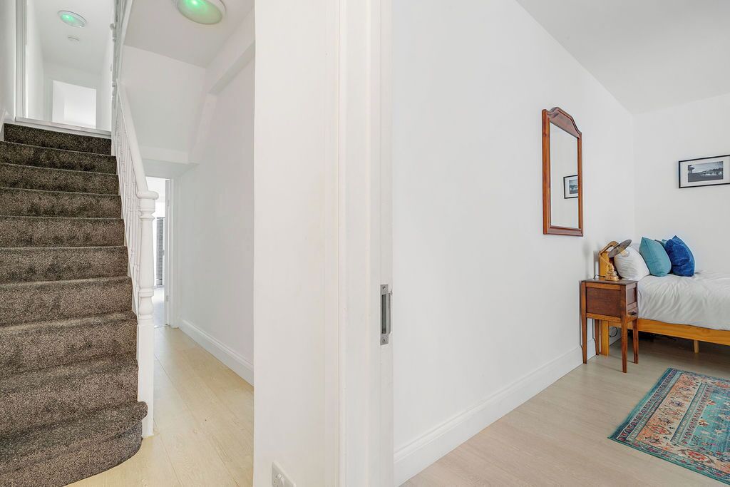 A bedroom with a bed, a nightstand, a mirror, and a carpeted staircase.