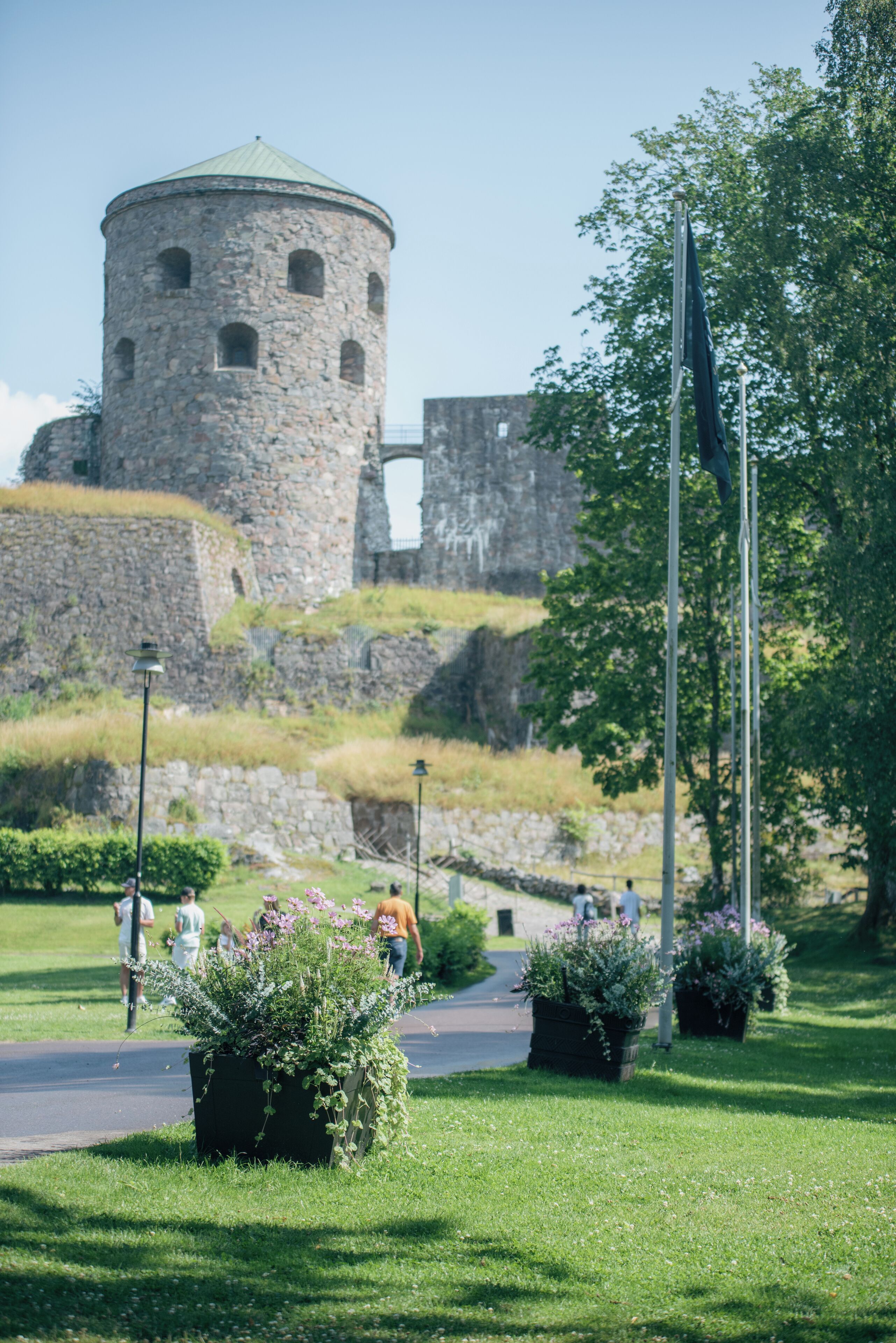 A stone tower with a circular top, surrounded by greenery and a paved path.