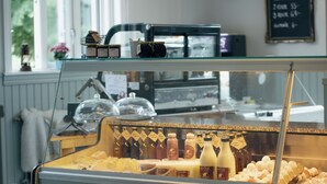 Una vitrina con diversos alimentos, un reloj y un menú en pizarra en un café.