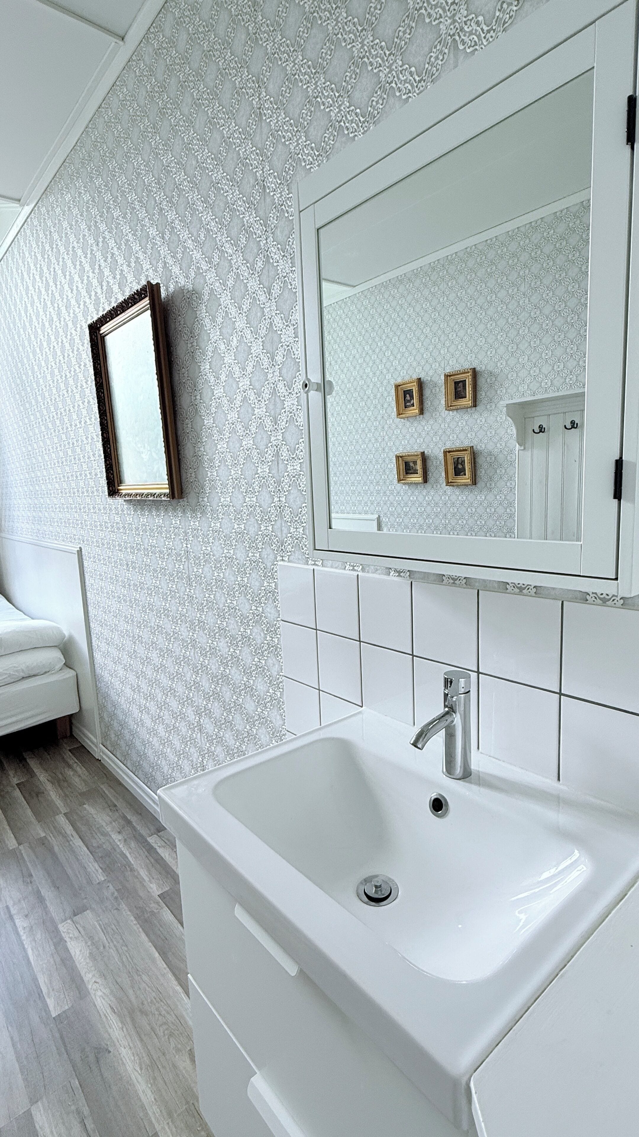 A bathroom with a white sink, a mirror, and patterned wallpaper.
