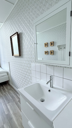Un baño con lavamanos blanco, un espejo y papel tapiz estampado.