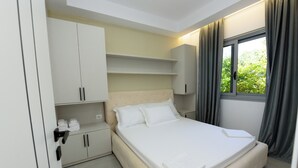 A neatly arranged bedroom with a bed, built-in cabinets, and a window with curtains. - Vila 42 (Vlore)