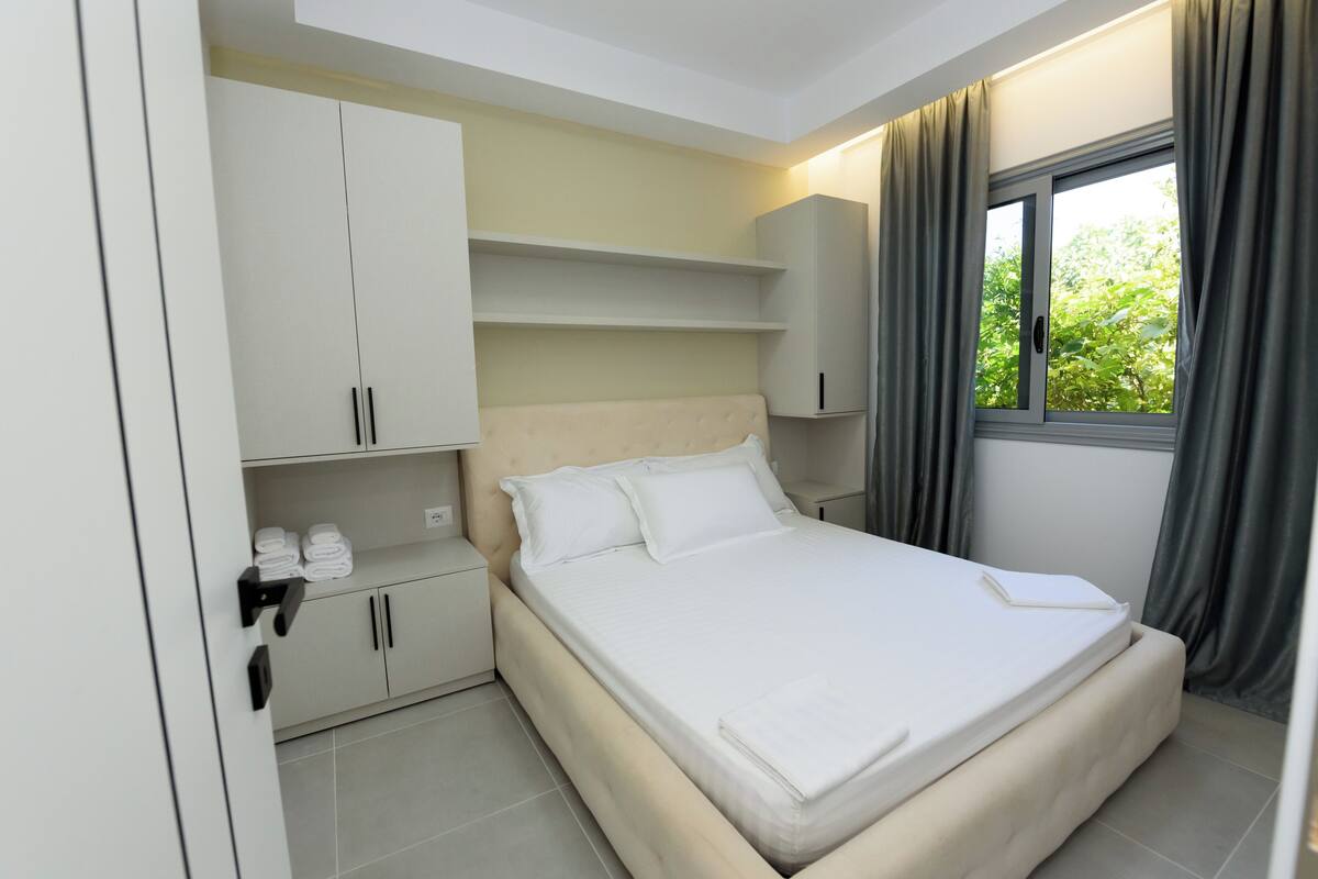 A neatly arranged bedroom with a bed, built-in cabinets, and a window with curtains.