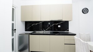 A compact kitchen with a black marble backsplash, a stainless steel refrigerator, and a white dining area. - Vila 42 (Vlore)