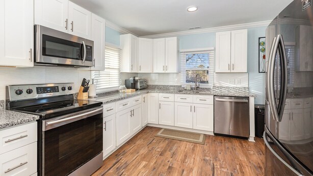 A modern kitchen with white cabinets, stainless steel appliances, granite countertops, and a wooden floor. - Modern And Cozy House In The Heart Of Hillsborough (Hillsborough)