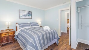 A bedroom with a bed, bedside lamps, a wooden nightstand, and a door leading to another room. - Modern And Cozy House In The Heart Of Hillsborough (Hillsborough)