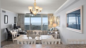 A modern dining area with a chandelier, a large window with a view, and a seating arrangement. - 2BR Atlantis, Family Friendly, 16th fl Oceanfront Views, Outdoor Oceanfront Pool (Ocean City)