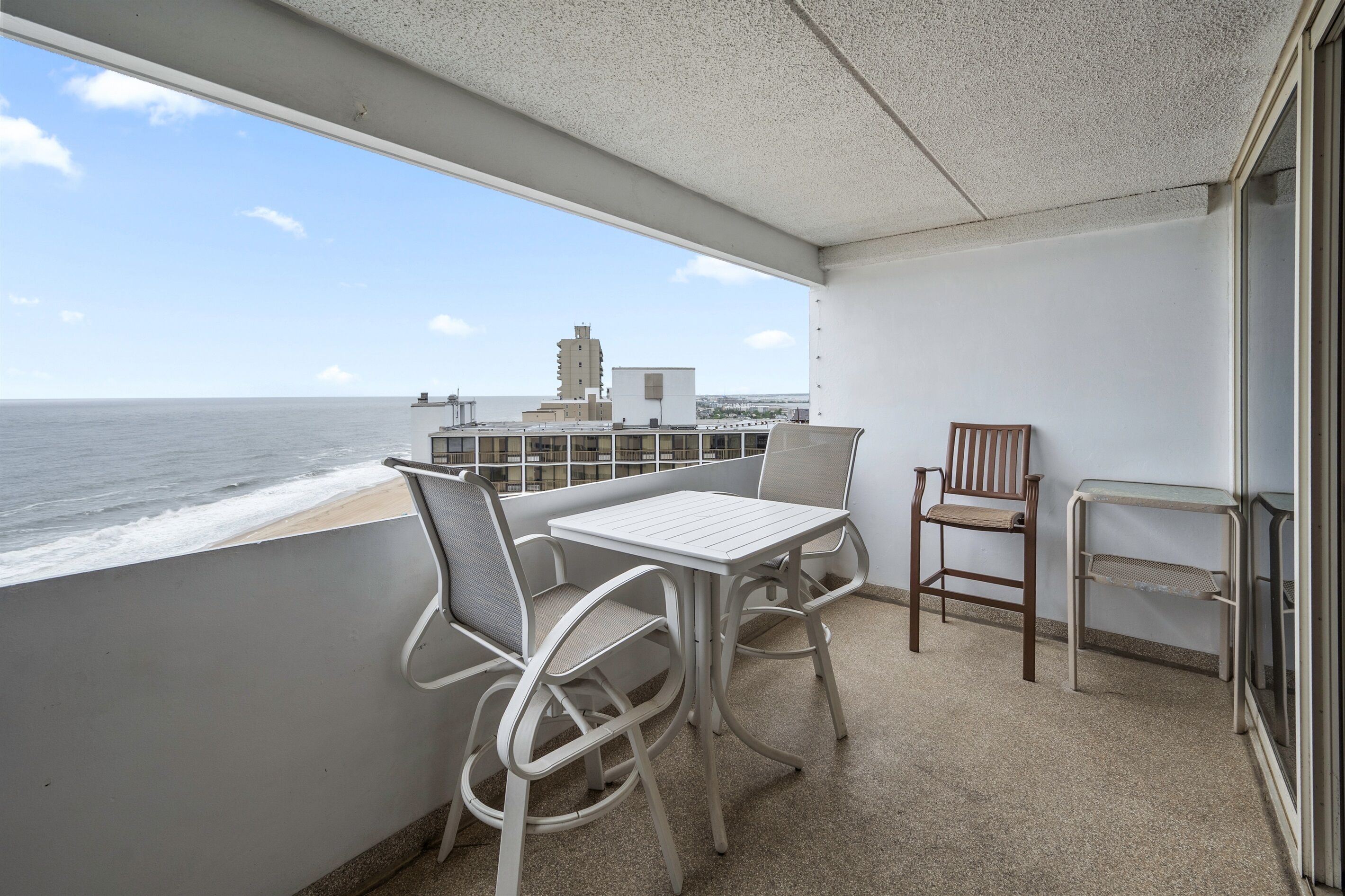A balcony with a table and chairs, a view of the sea, and a building in the background.