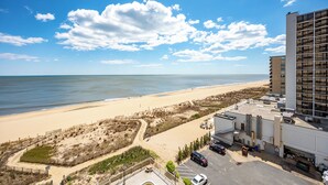A beachfront hotel with a sandy beach, a parking lot, and a building with multiple floors. - 2BR Atlantis, Family Friendly, 16th fl Oceanfront Views, Outdoor Oceanfront Pool (Ocean City)