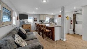 Eine moderne Küche mit Kochinsel, einem Essbereich mit Sofa und Stühlen sowie einem an der Wand montierten Flachbildfernseher.