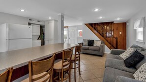 Eine moderne Küche mit weißen Schränken, einer Holz-Insel mit Stühlen und einem grauen Sofa im Wohnbereich.