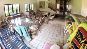 A spacious living area with a dining table surrounded by chairs, a staircase leading to an upper level, and a view of greenery outside. - Casa Grande Lomas de Cocoyoc (Fraccionamiento Lomas de Cocoyoc)