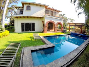 A two-story house with a swimming pool, a covered patio, and a well-maintained lawn.