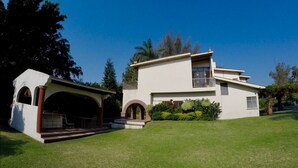 A modern two-story house with a covered patio, a small garden, and a clear blue sky. - Casa Grande Lomas de Cocoyoc (Fraccionamiento Lomas de Cocoyoc)