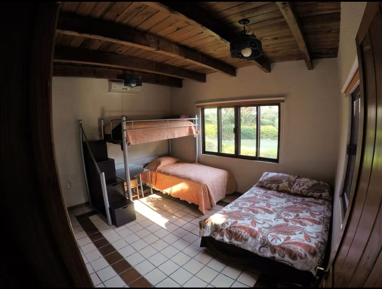 Une chambre avec un lit superposé, un escalier et une fenêtre donnant sur un paysage verdoyant.