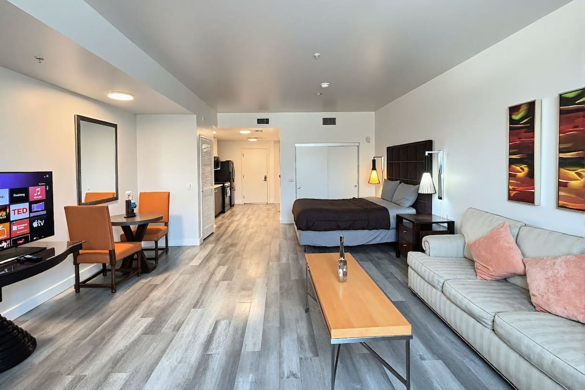 A modern hotel room with a bed, sofa, TV, desk, and a dining area.